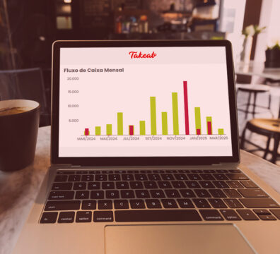 Imagem de um laptop exibindo um gráfico de fluxo de caixa mensal da Takeeat, com um copo de café ao lado, ideal para análises financeiras.