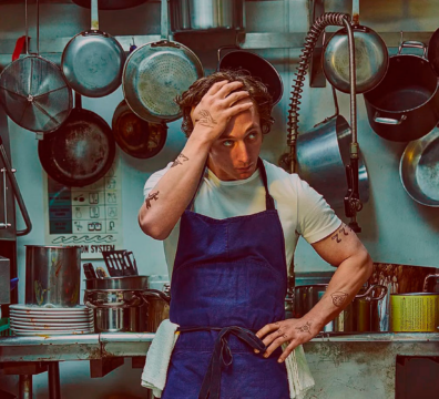 chef de restauante sério e pensativo, usando avental na cozinha com panelas penduradas ao fundo, demonstrando concentração e preocupação com a eficiência operacional de seu restaurante